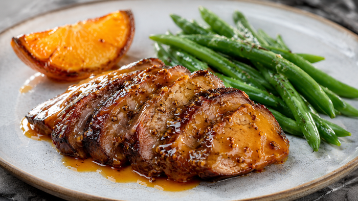 Sliced honey mustard oyster blade roast with a glossy orange wholegrain mustard glaze in a roasting tray